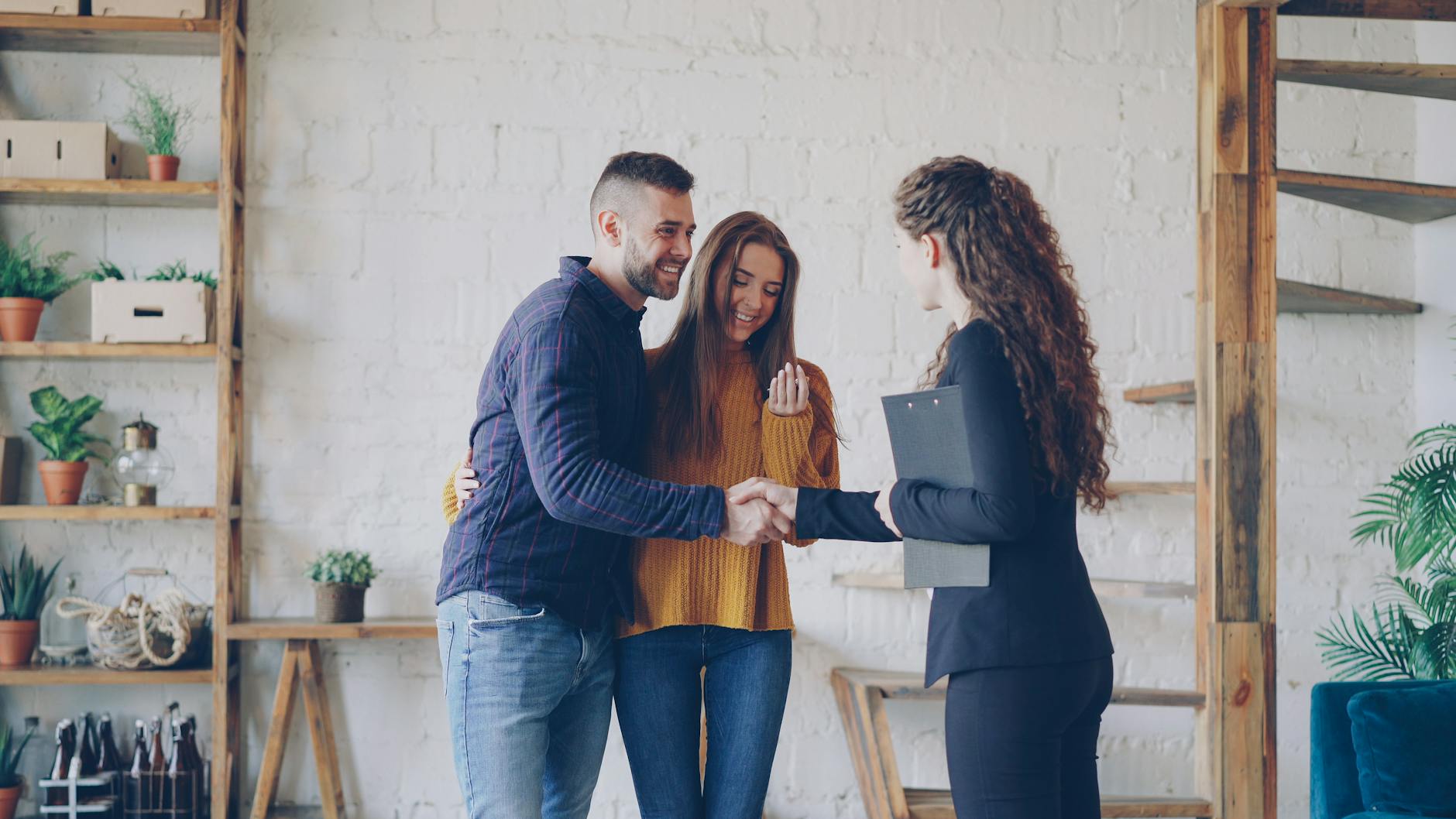A real estate agent shakes hands with a happy couple in a stylish modern living space.